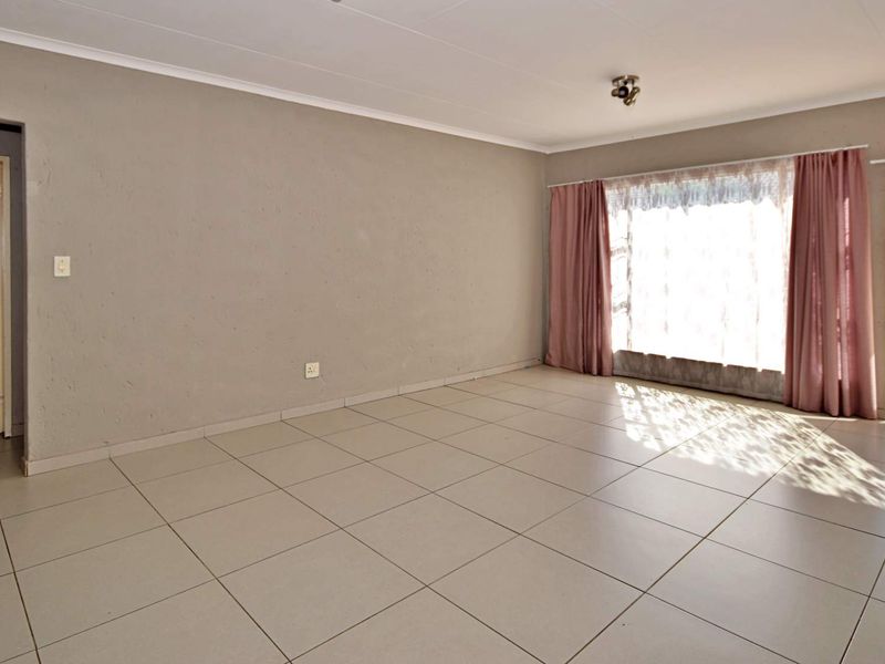 Spacious, empty living room featuring neutral tiled flooring, a large window with curtains, and direct access to an outdoor balcony area.