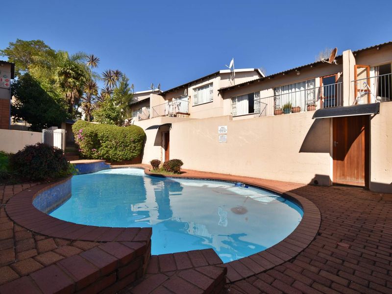 A communal swimming pool area featuring brick paving and a retaining wall, set against the exterior facade of an apartment complex.