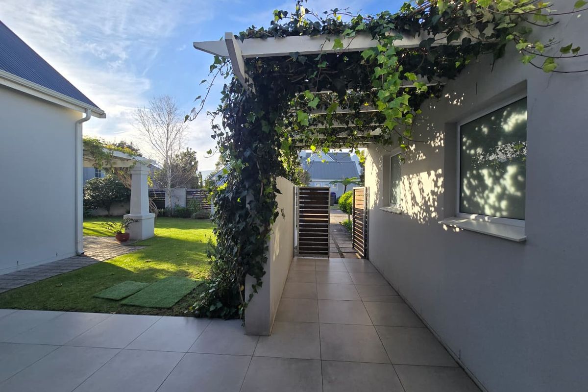 A covered patio area featuring a pergola with climbing greenery, tiled flooring, and a gated walkway leading to the garden.