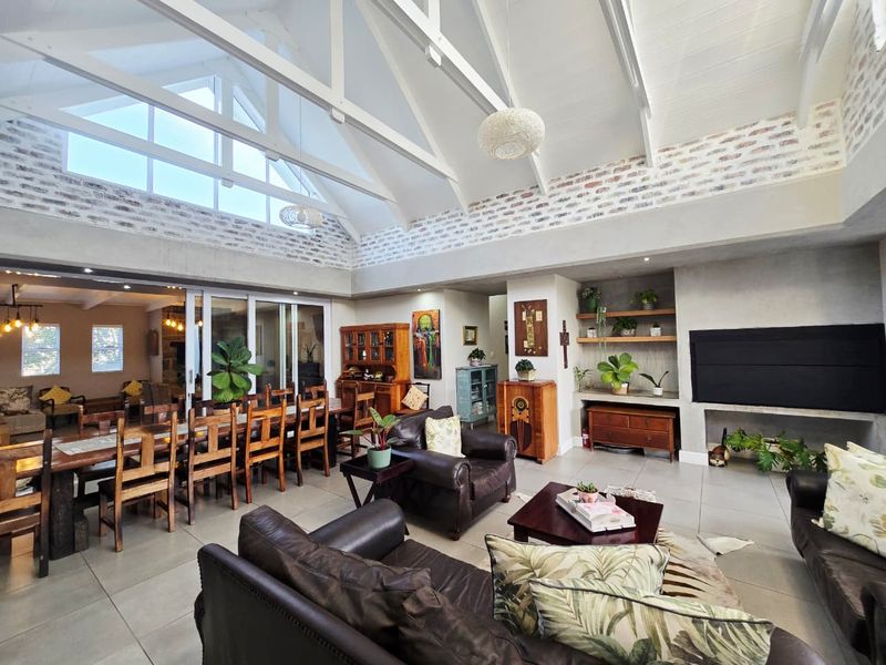 Spacious open-plan living and dining area featuring a high vaulted ceiling with exposed trusses, brick accents, and large sliding doors leading to an adjacent space.