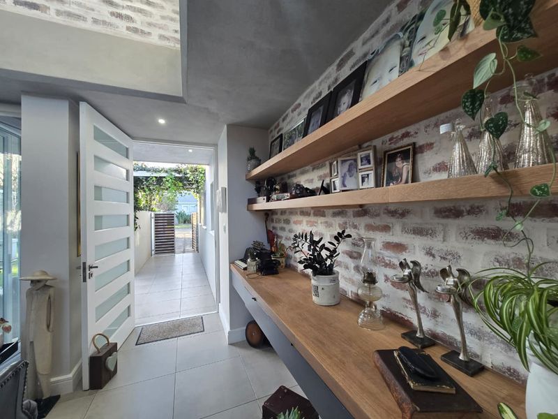 Modern entry hall featuring an exposed brick feature wall, custom built-in timber shelving and desk, tiled flooring, and a contemporary glass-panelled door.