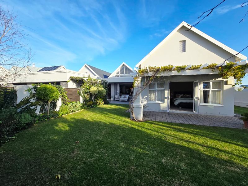 A well-maintained rear garden featuring a paved patio area, a pergola, and direct access to the home through french doors.