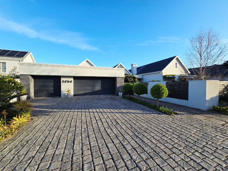 A well-maintained front exterior featuring a double garage, paved driveway, and modern boundary wall with solar panels visible on the roof.