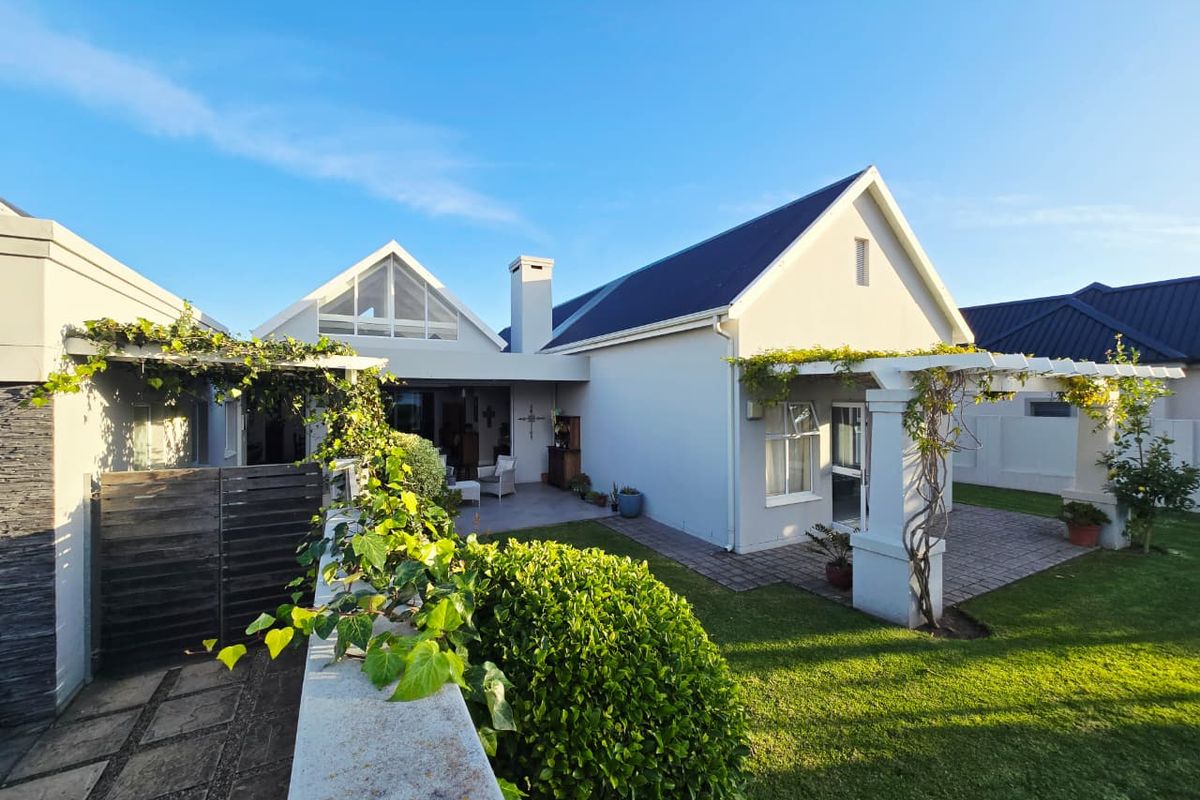 Rear view of the house featuring a paved patio, timber pergola, well-maintained garden, and a prominent chimney stack under a pitched roof.