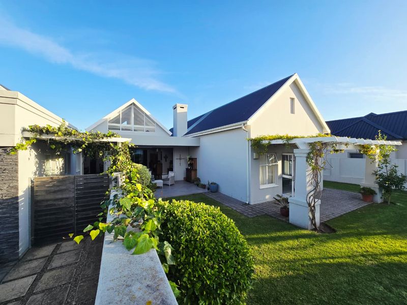 Rear view of the house featuring a paved patio, timber pergola, well-maintained garden, and a prominent chimney stack under a pitched roof.