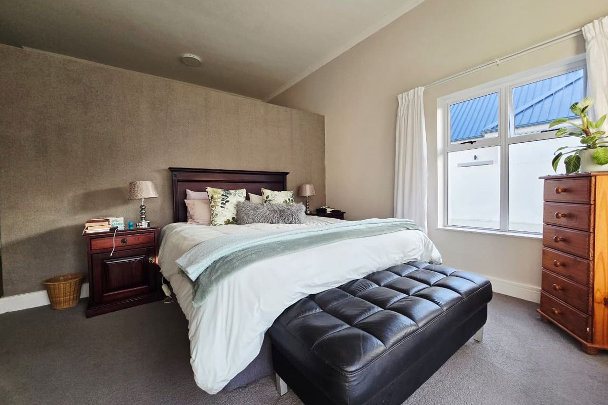 A well-lit bedroom featuring neutral wall tones, carpeted flooring, and a large window providing natural light.