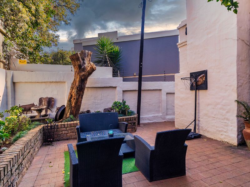 A paved outdoor patio area featuring brick retaining walls, perimeter security fencing, and a private courtyard setting.