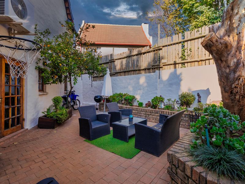 A private paved patio area featuring raised brick planter beds, a timber boundary fence, and direct access to the home through timber-framed glass doors.
