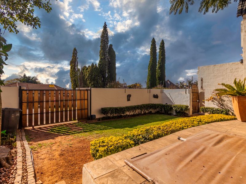 A private rear garden featuring a paved patio area, lawn, perimeter wall with electric fencing, and secure wooden driveway and pedestrian gates.