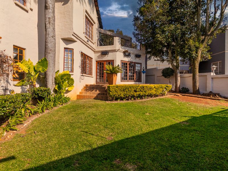Rear view of the property featuring a landscaped garden, raised patio area, and traditional timber-framed windows and doors.