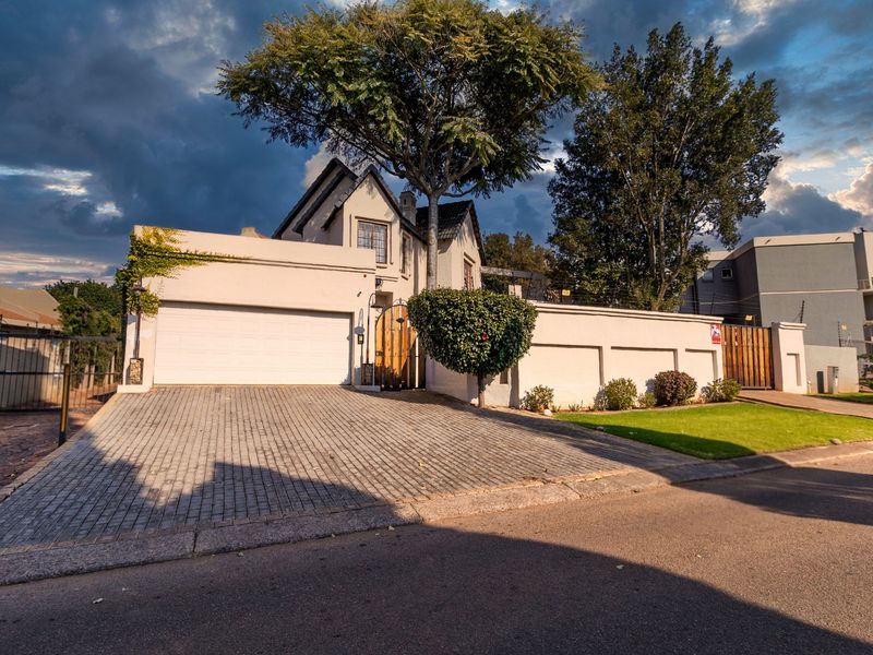 Front elevation of a duet property featuring a paved driveway, double garage, and secure boundary wall with electric fencing.