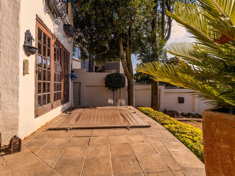 A covered patio area featuring tiled flooring, wooden french doors, and a wall-mounted water feature, providing a functional outdoor space.