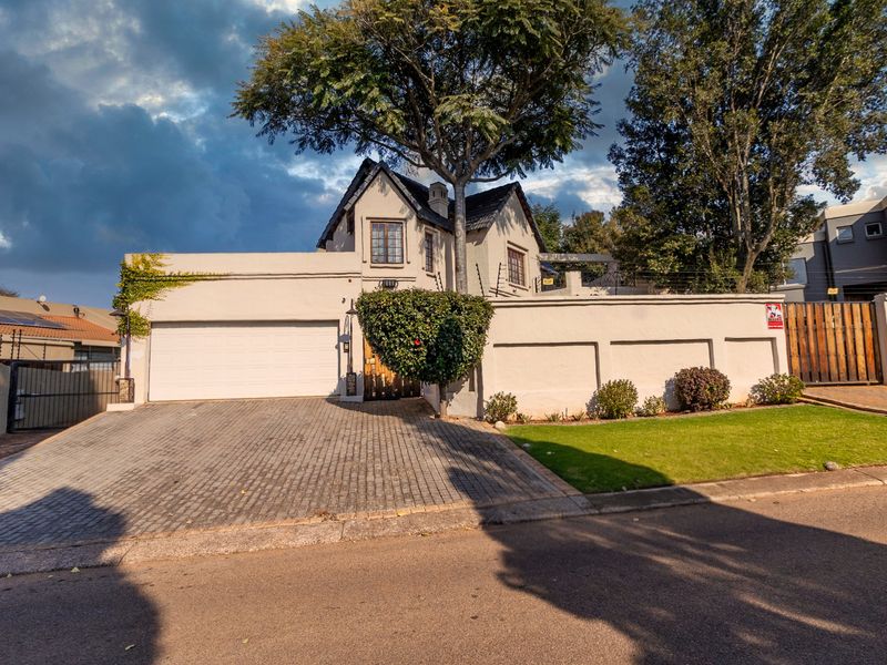 Front elevation of a duet property featuring a paved driveway, double garage, secure boundary wall with electric fencing, and a well-maintained front garden.