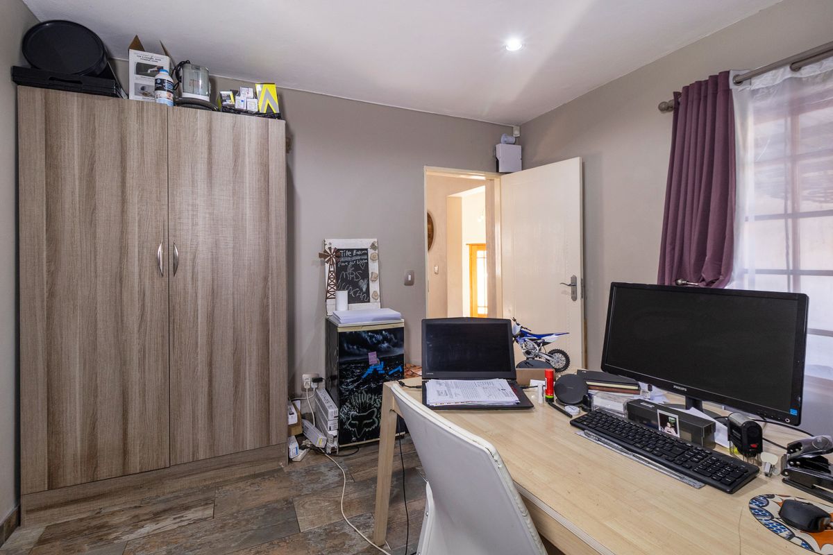 A functional bedroom featuring tiled flooring, a built-in wardrobe, and recessed lighting, currently utilized as a home office space.