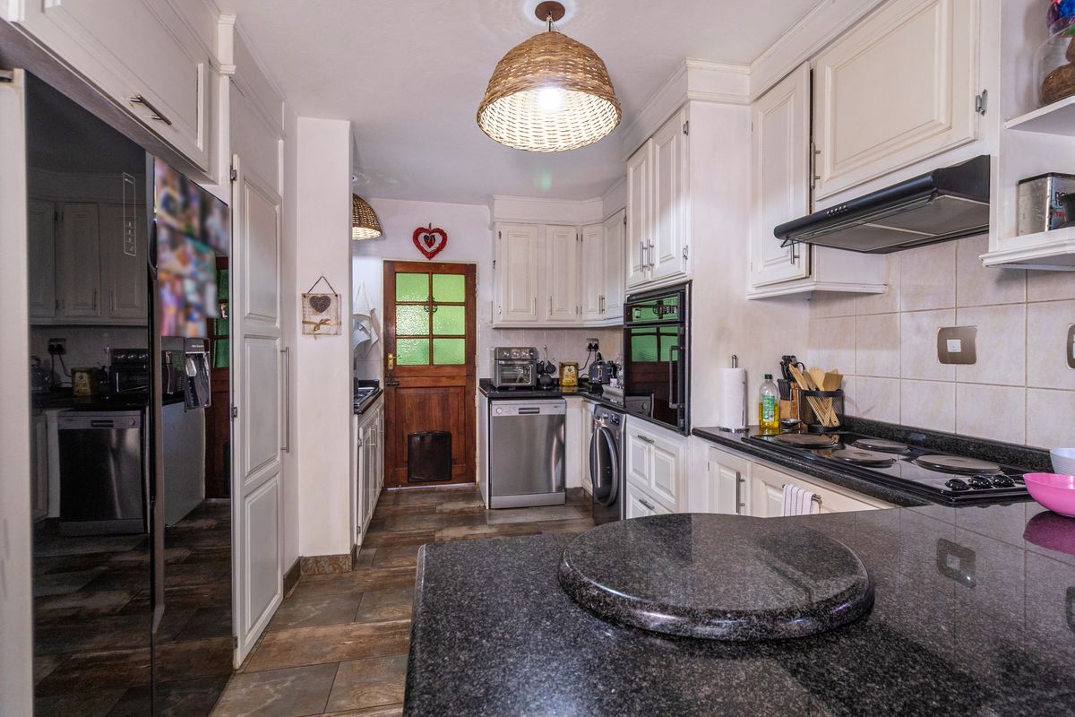A functional kitchen featuring granite countertops, built-in cabinetry, an integrated oven, and an extractor fan, with direct access to an exterior timber door.