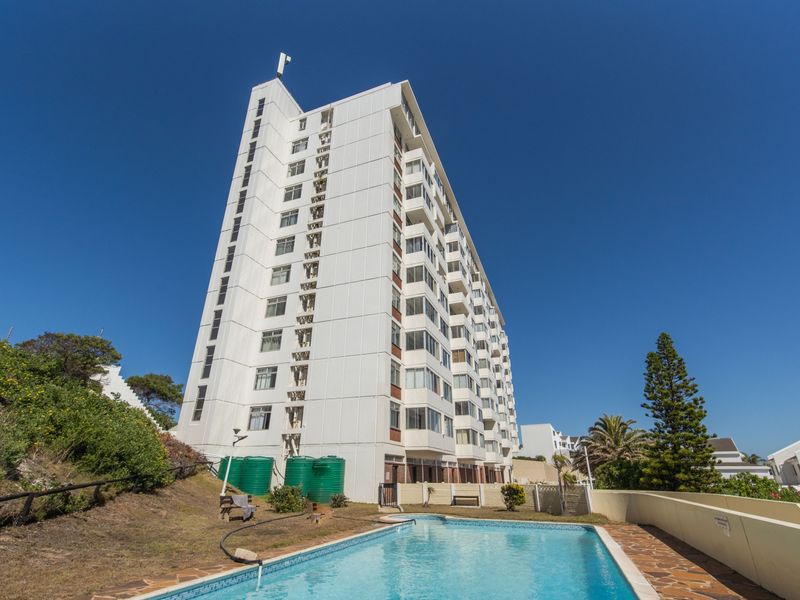 Exterior view of a high-rise apartment building featuring a swimming pool, paved deck area, and external water storage tanks.