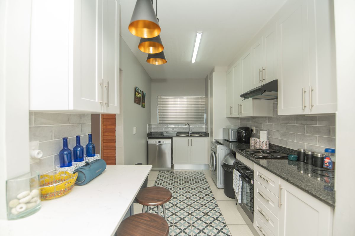 Modern galley-style kitchen featuring white cabinetry, granite countertops, subway tile backsplash, and integrated appliances with stylish pendant lighting.