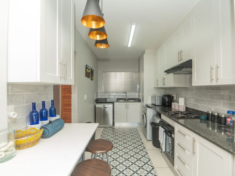Modern galley-style kitchen featuring white cabinetry, granite countertops, subway tile backsplash, and integrated appliances with stylish pendant lighting.
