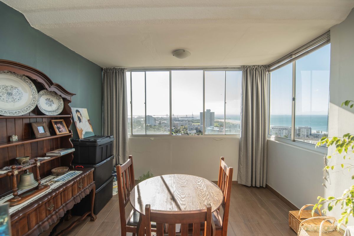 A bright living area featuring large windows with expansive coastal and city views, laminate flooring, and a neutral color palette.
