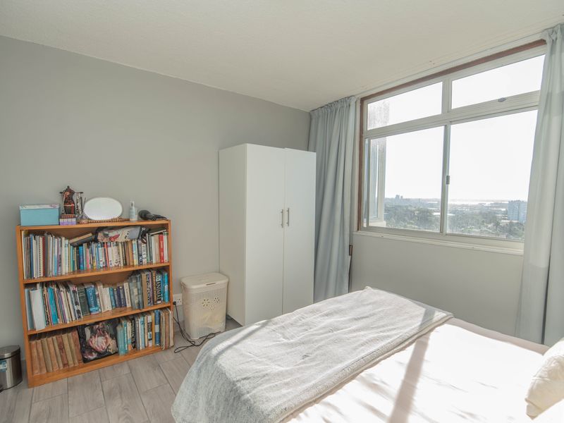 A bedroom featuring light-toned laminate flooring, a large sliding window with natural light, and neutral wall finishes.