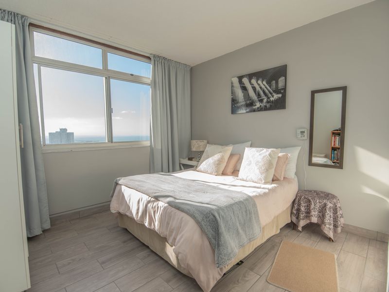 A bright bedroom featuring large windows with ocean views, neutral tiled flooring, and a built-in wardrobe.