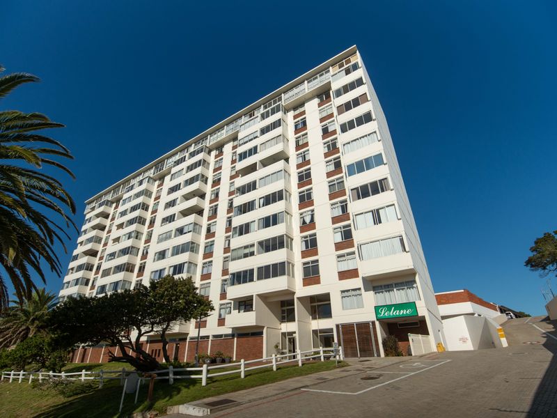 A low-angle exterior view of the Lelane apartment building, showcasing its multi-story facade, balconies, and paved driveway entrance.