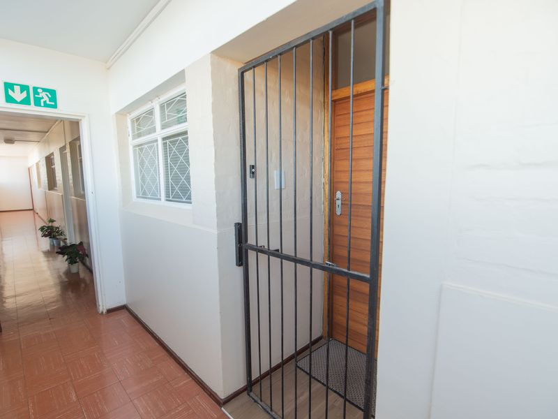 A clean apartment hallway featuring tiled flooring, a secure metal gate, and a wooden entrance door.