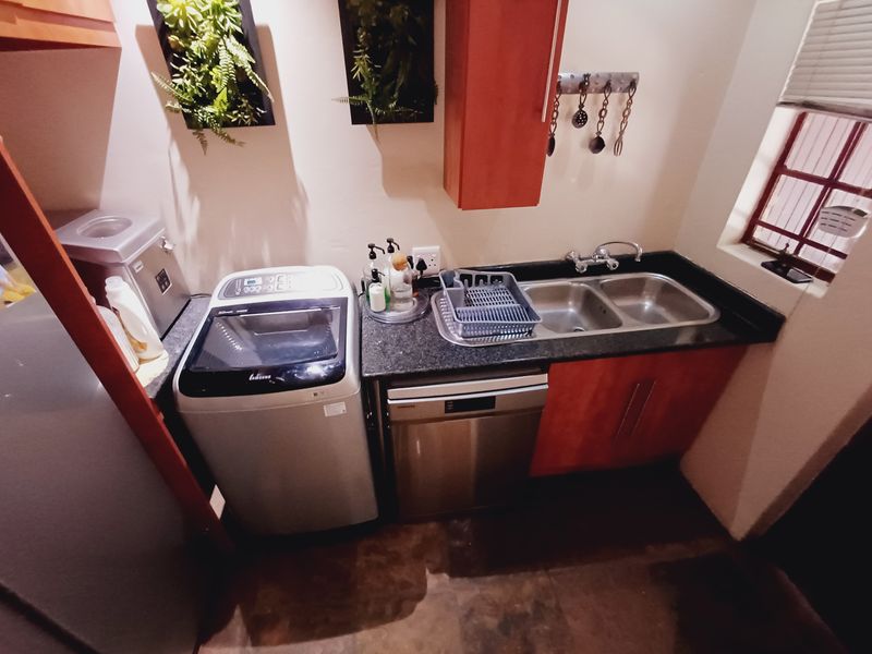 A functional laundry area featuring a double bowl sink, granite countertops, built-in cabinetry, and space for a dishwasher and washing machine.