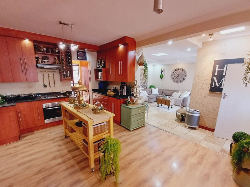 Open-plan kitchen and living area featuring warm-toned cabinetry, granite countertops, integrated appliances, and a seamless transition between tiled and laminate flooring.