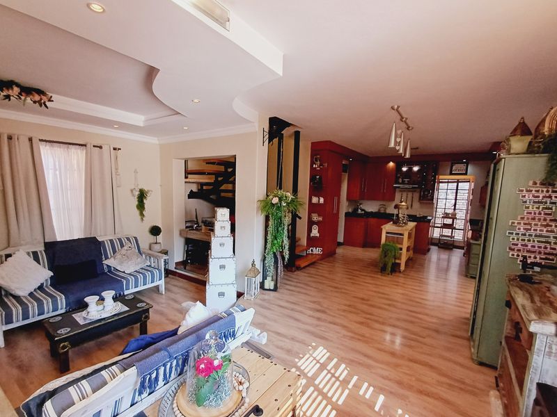 Spacious open-plan living area featuring laminate flooring, recessed ceiling details, and a connected kitchen with built-in cabinetry and staircase access.