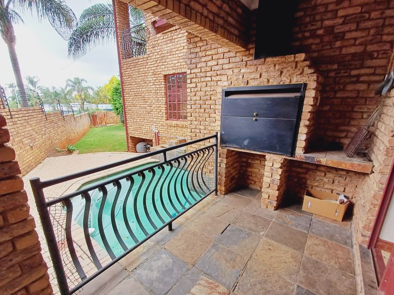 Covered patio area featuring a built-in braai, stone tile flooring, and a wrought iron railing overlooking the swimming pool and garden.