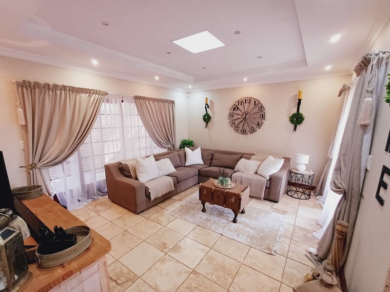 A spacious living room featuring tiled flooring, a central skylight, recessed ceiling lighting, and large sliding glass doors providing natural light.