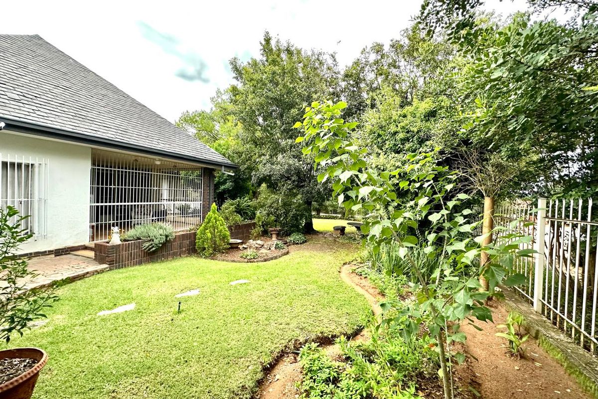 A view of the rear garden featuring a lawn, established trees, a brick planter, and a covered patio area with security bars.