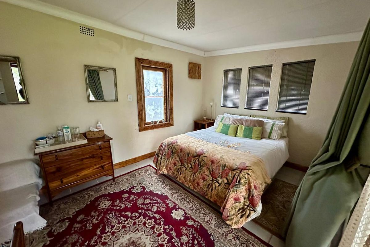 A bedroom featuring tiled flooring, timber-framed windows with venetian blinds, and a central ceiling light fixture, showing signs of wear on the walls.