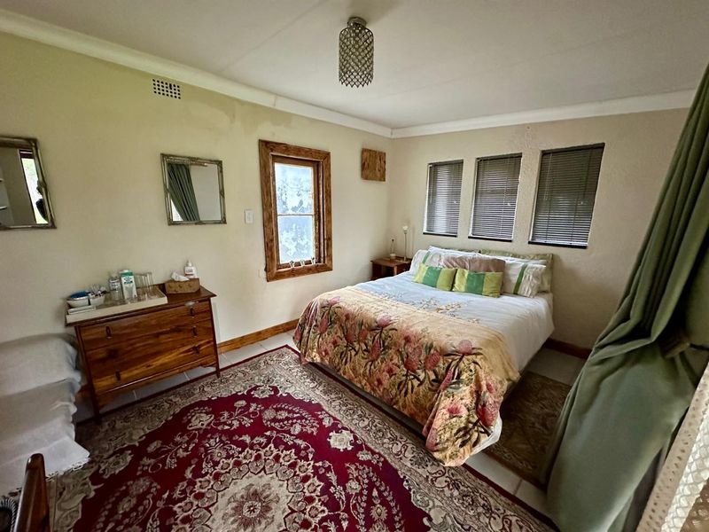 A bedroom featuring tiled flooring, timber-framed windows with venetian blinds, and a central ceiling light fixture, showing signs of wear on the walls.