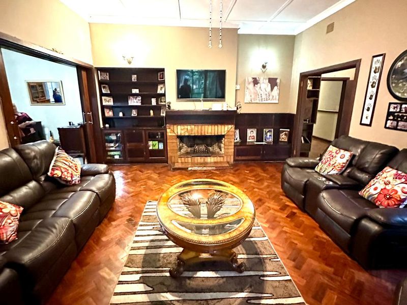 Spacious living room featuring classic parquet flooring, a central brick fireplace, and built-in cabinetry, offering a warm and traditional atmosphere.