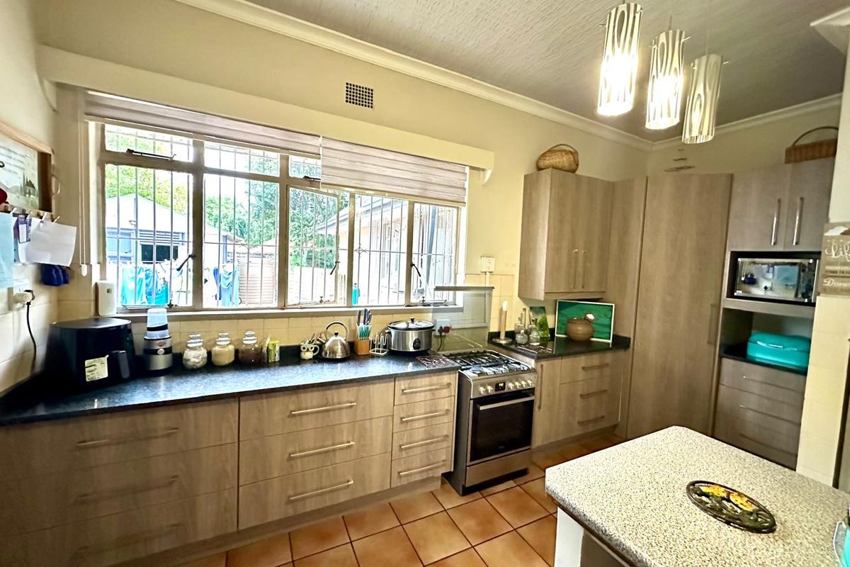 A functional kitchen featuring light wood-finish cabinetry, dark laminate countertops, a gas stove with oven, and tiled flooring with ample natural light.