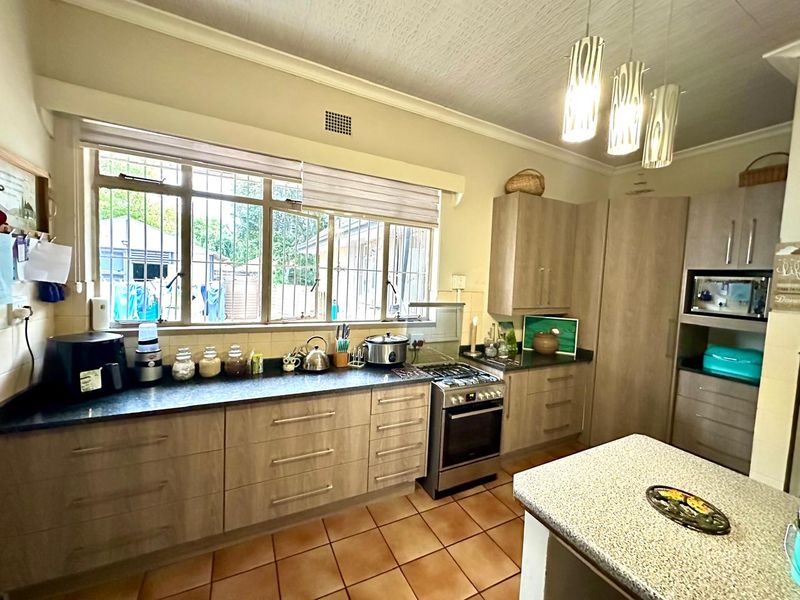 A functional kitchen featuring light wood-finish cabinetry, dark laminate countertops, a gas stove with oven, and tiled flooring with ample natural light.