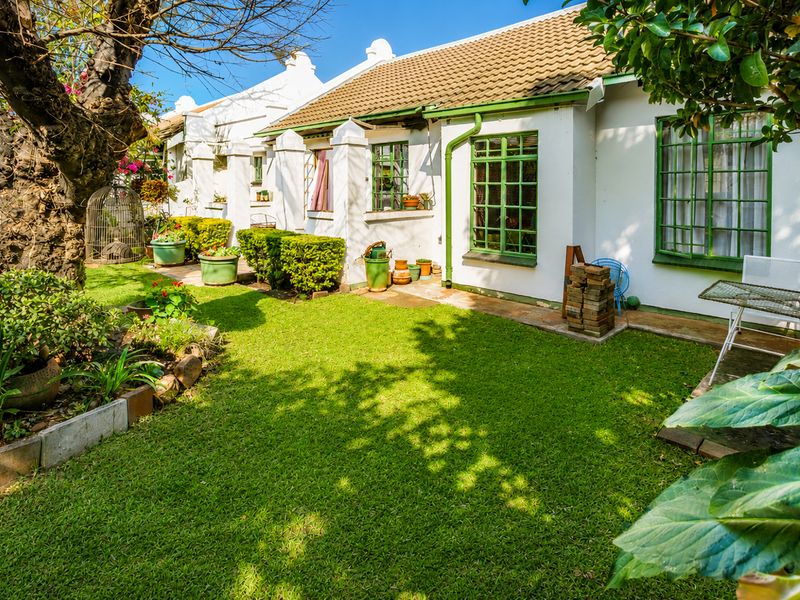 A well-maintained rear garden area featuring a lawn, paved walkway, and the rear elevation of a retirement village unit with green-framed windows.