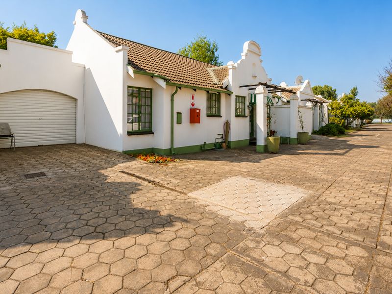 Front elevation of a retirement village unit featuring a roller garage door, paved driveway, and classic Cape Dutch style architectural details.
