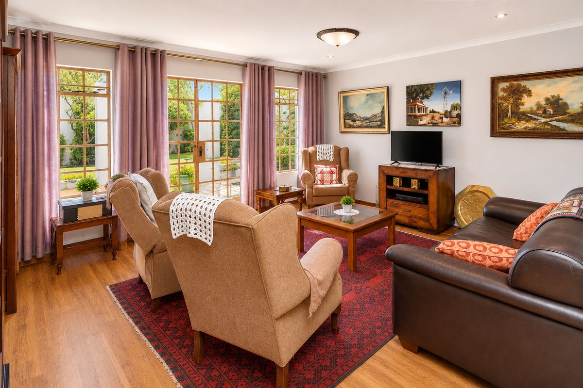 A well-maintained living room featuring laminate flooring, large windows, and french doors providing direct access to the garden area.