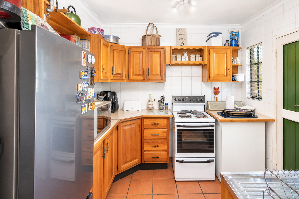 A functional kitchen featuring timber cabinetry, tiled splashbacks, and a freestanding oven, offering a classic layout with practical storage and workspace.