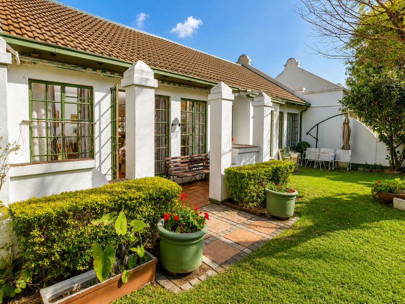 A well-maintained rear exterior view of a retirement village unit featuring a paved patio, concrete pillars, and access to a private garden.