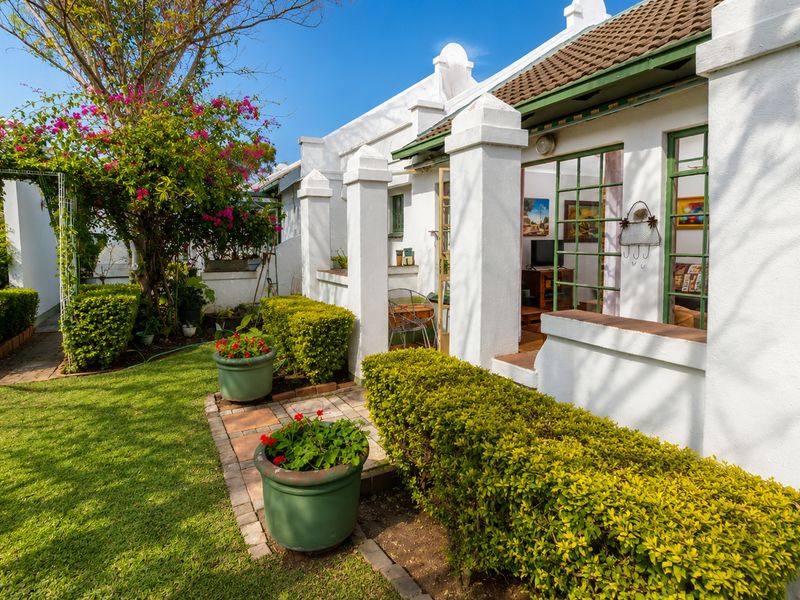 A well-maintained rear exterior view of a retirement village unit featuring a paved patio, landscaped garden, and classic white plastered architecture.