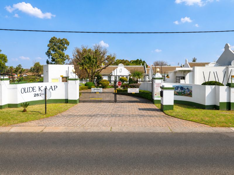 Front entrance view of Oude Kaap retirement village, featuring a secure gated access point, paved driveway, and well-maintained boundary walls with electric fencing.