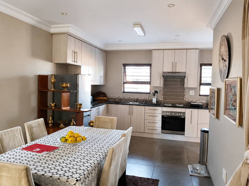 Open-plan kitchen and dining area featuring light-toned cabinetry, built-in oven, hob, extractor fan, and tiled flooring throughout.