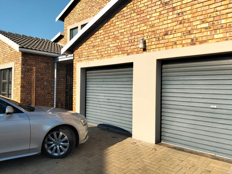 Front view of the property featuring a double garage with roller doors, brick exterior, and a paved driveway.