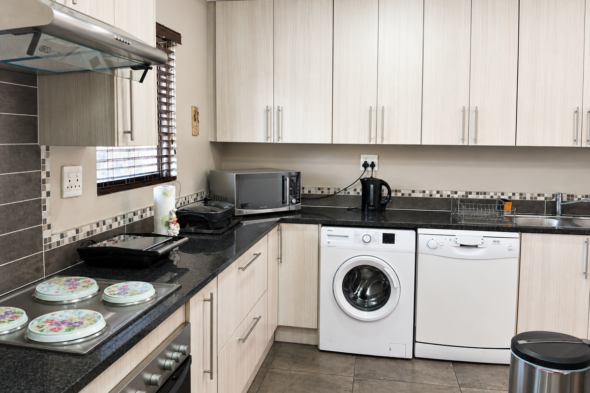 A functional kitchen featuring light wood-finish cabinetry, dark granite countertops, a mosaic tile backsplash, and integrated stainless steel appliances.