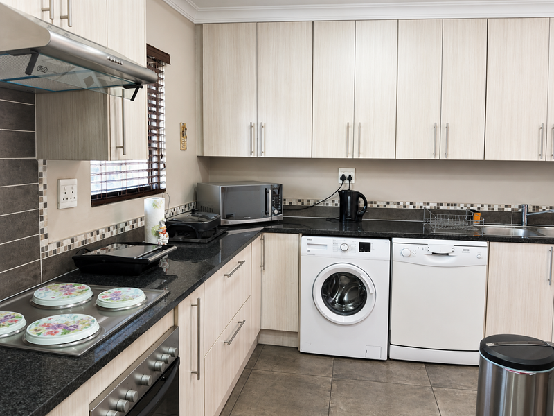 A functional kitchen featuring light wood-finish cabinetry, dark granite countertops, a mosaic tile backsplash, and integrated stainless steel appliances.