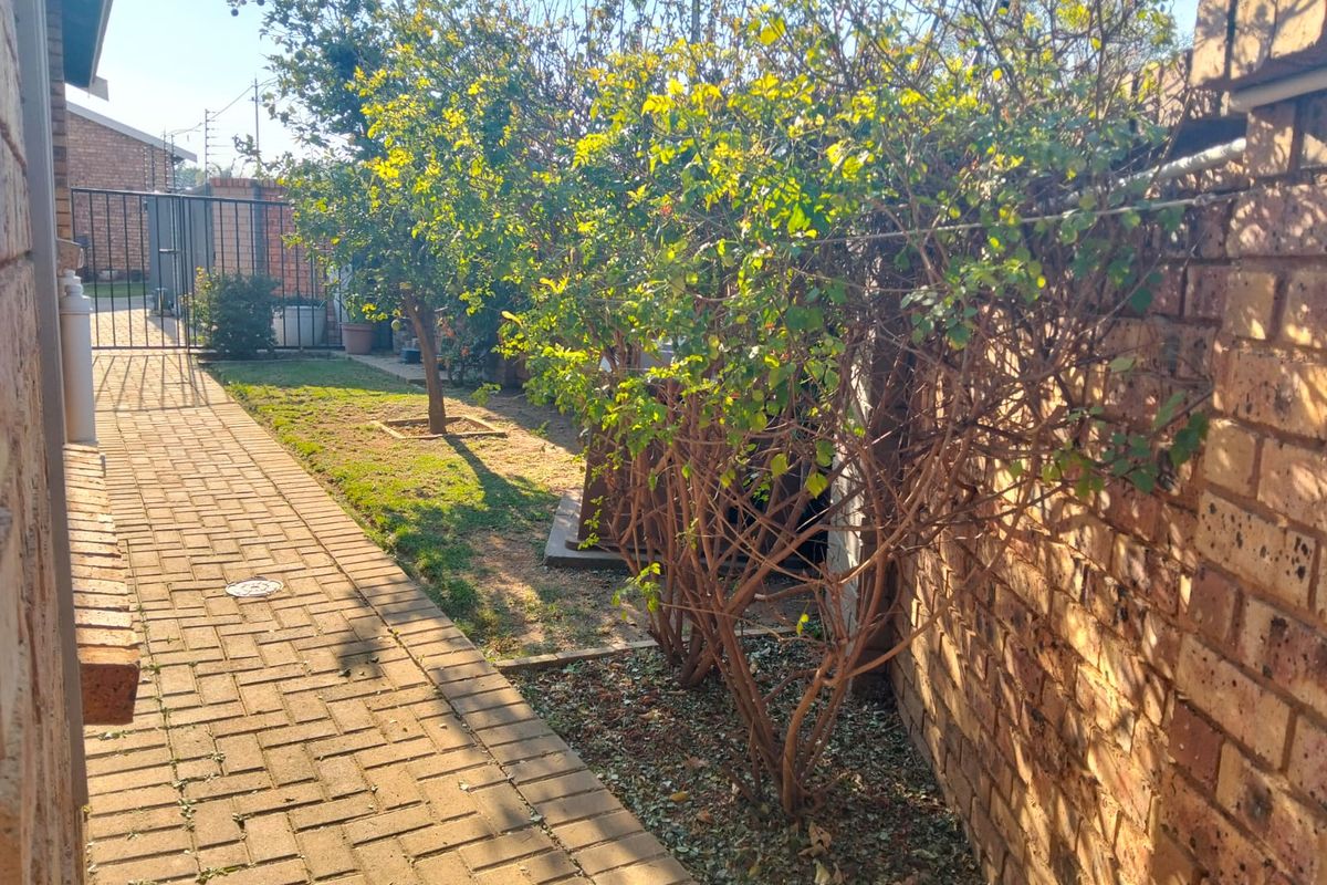 A side garden pathway featuring brick paving, a brick boundary wall, and a metal security gate leading to the rear outdoor area.